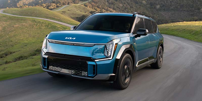 Blue Kia EV9 on a winding road with green rolling hills in the background