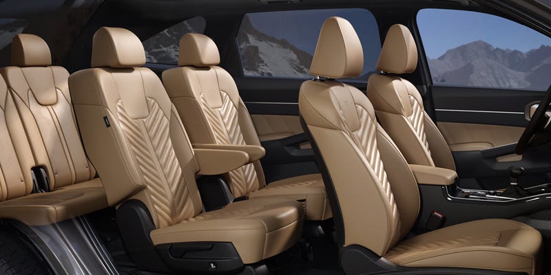 Interior of a car with three rows of tan seats. The front seats have armrests; mountains are visible outside the windows