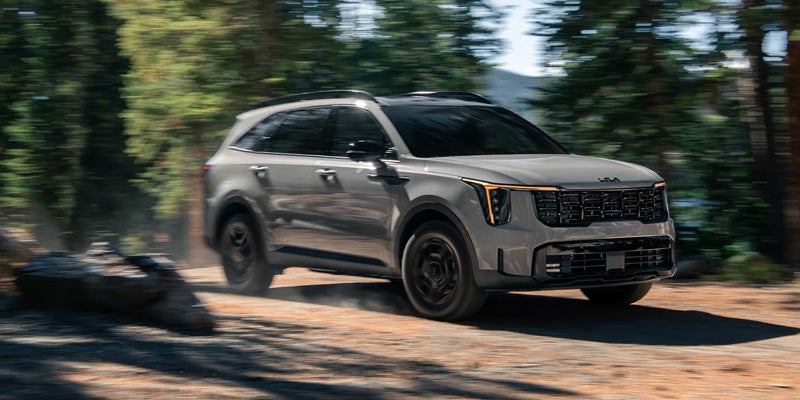Gray Kia Sorento SUV kicks up dust driving down a dirt road in a forest